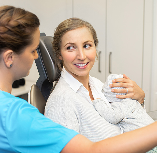 Frau mit Baby auf Zahnarztstuhl